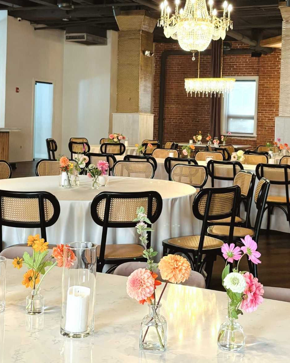 A wedding reception setup with tables decorated with floral bud vase centerpieces, featuring a variety of wildflowers.