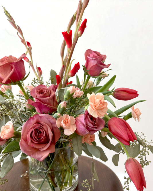 Floral arrangement with pink and red flowers in a clear vase on a white background