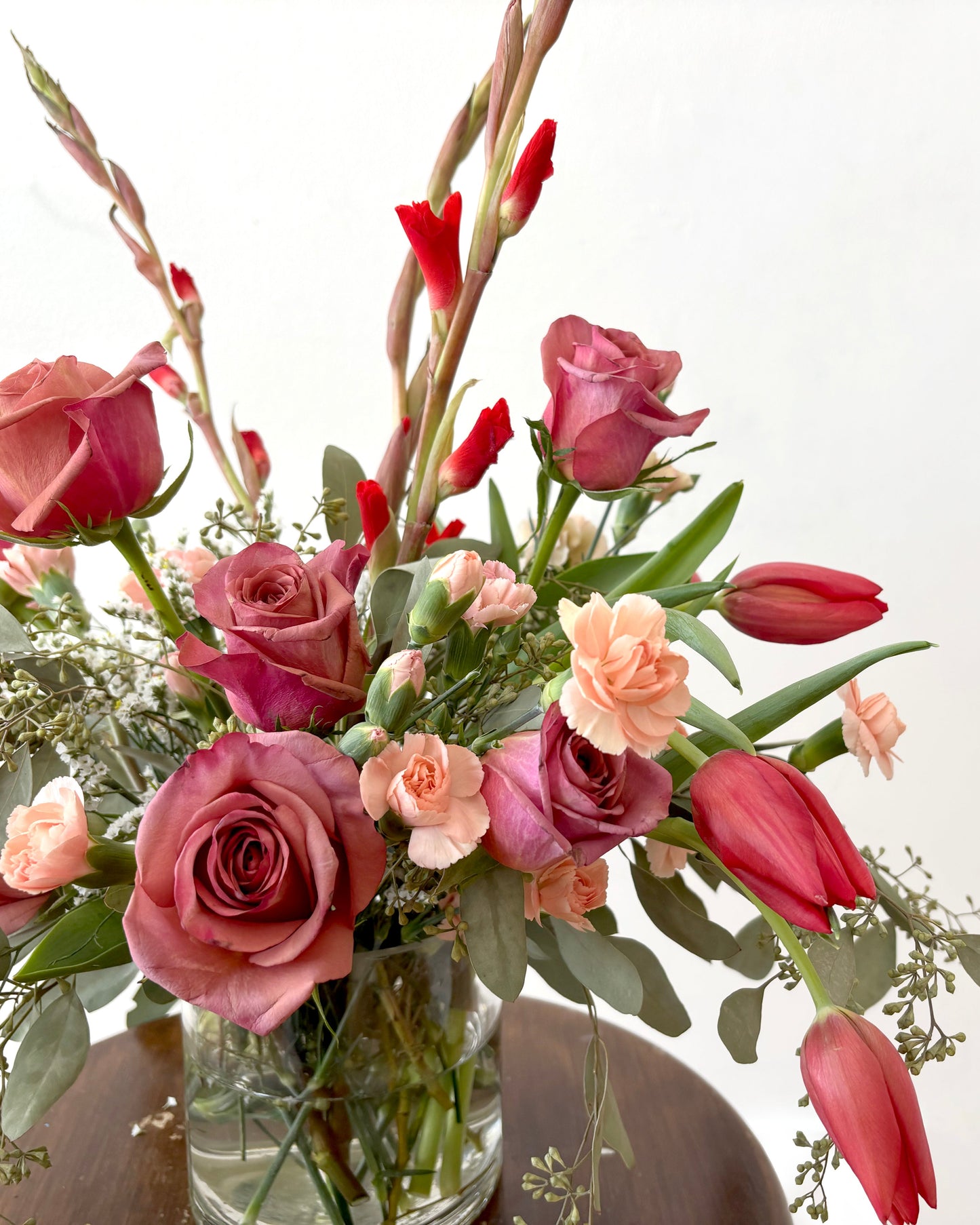 Floral arrangement with pink and red flowers in a clear vase on a white background